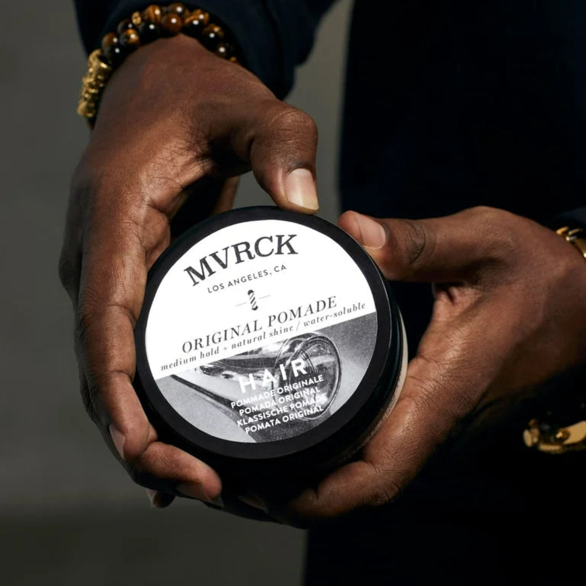 Person holding a container of MVRCK Original Pomade against a dark background