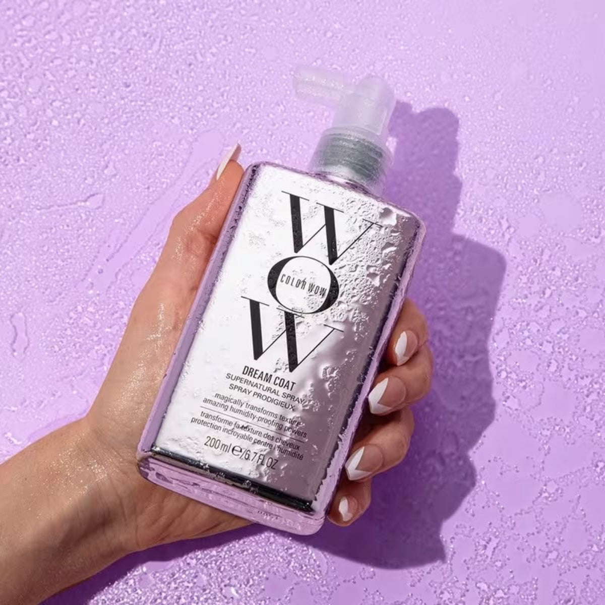 Hand holding a bottle of Color Wow Dream Coat product against a purple background