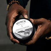 Person holding a container of MVRCK Original Pomade against a dark background