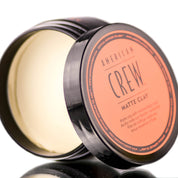 A container of American Crew Matte Clay hair styling product, with the lid off, showing the white clay inside.