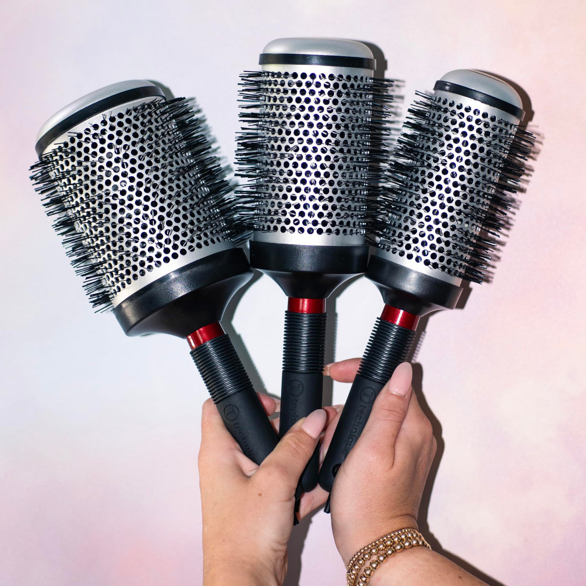 Three hairbrushes held by a person against a light background