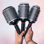 Three hairbrushes held by a person against a light background