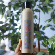 Hand holding a bottle of Davines hair product with a blurred green leafy background