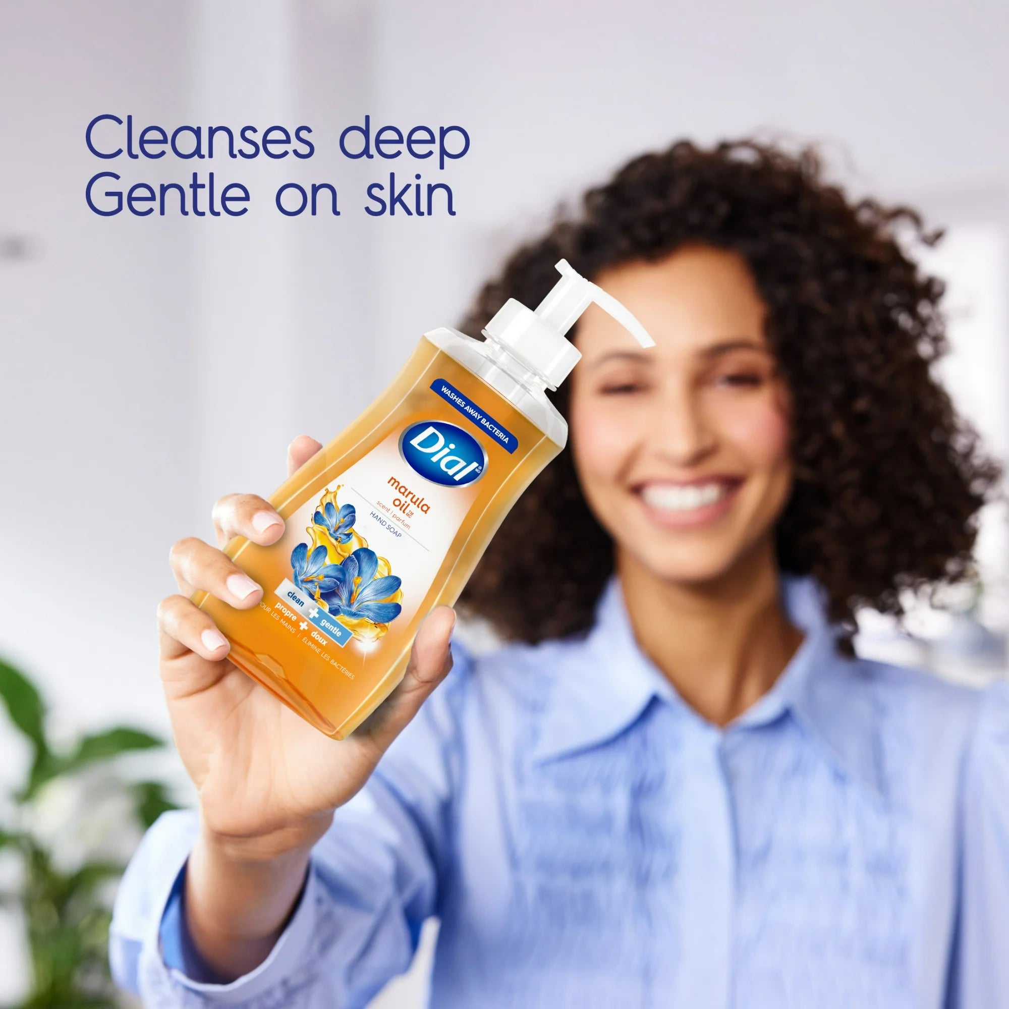 Woman holding a bottle of Dial manna oil with text 'Cleanses deep, Gentle on skin' on a blurred background