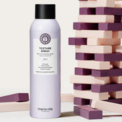 Maria Nila texture spray bottle next to a stack of wooden blocks