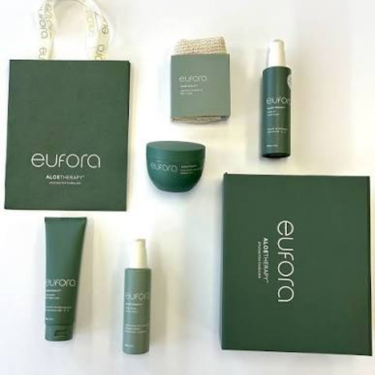 A skincare gift set from euforia Aloe Therapy arranged on a white background, including a dark green shopping bag, a large dark green box, several green skincare bottles and tubes, and a small beige textured item.