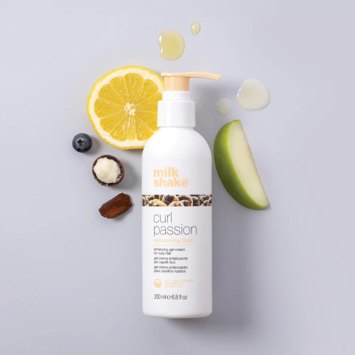Bottle of 'milk shake' curl passion product with lemon, blueberry, and avocado on a light gray background
