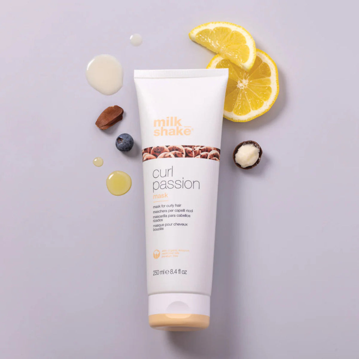 Tube of 'milk shake' curl passion product with lemon slices and berries on a light purple background