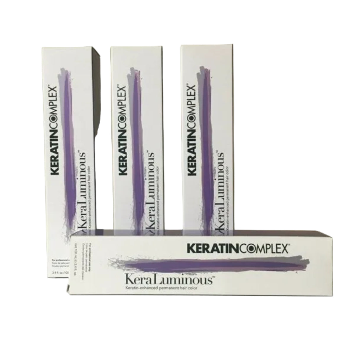 Three white boxes of KeraTIN COMPLEX KeraLuminous permanent hair color are arranged on a light surface against a beige background, with one box placed in front.