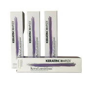 Three white boxes of KeraTIN COMPLEX KeraLuminous permanent hair color are arranged on a light surface against a beige background, with one box placed in front.
