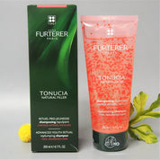 Rene Furterer Paris Tonucia Natural Filler Replumping Shampoo shown in a pink squeeze tube next to its dark green cardboard box, styled with yellow and green flower petals on a light gray background.